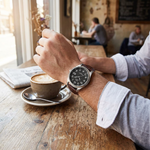 Men's leather strap watch worn at a cafe table